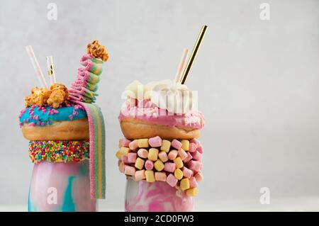 Freak-Shakes mit blauen und rosa Donuts, Marshmallow, Bakerüssen, Popcorn und Marmelade auf grauem Hintergrund; selektiver Fokus Stockfoto