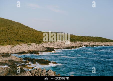 Felsige Küste in der Nähe Veslo Camping in Montenegro. Azurblaues Wasser, weiße Wellen treffen auf die Felsen, sonniger Sommertag, Luftdrohne Blick. Stockfoto