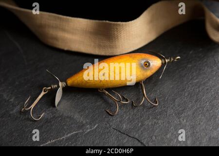 Ein Beispiel für einen alten South Bend Angelköder, oder Stecker, entwickelt, um Raubfische auf einem dunklen Schieferhintergrund neben einem alten Whicker ta angezeigt zu fangen Stockfoto