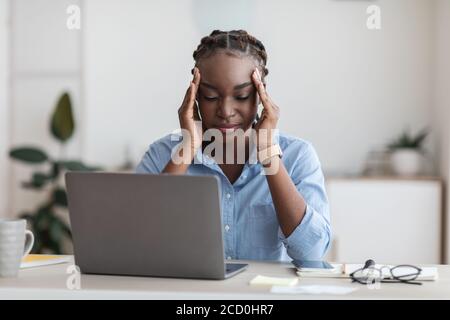 Überarbeitete schwarze Geschäftsfrau, die unter Kopfschmerzen im Büro leidet und Tempel massiert Stockfoto