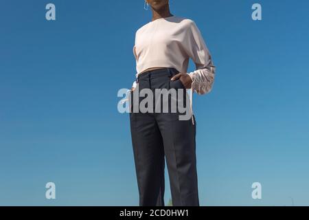 Nahaufnahme Porträt modische dunkelhäutige Mädchen, afrikanisches Mädchen in einer Bluse und Business-Hosen, posiert. Vor dem Hintergrund des blauen Himmels. Modisch b Stockfoto