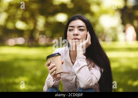 Kaffeepause Im Freien. Pensive Asiatische Mädchen Genießen Takeaway Trinken Im Park Stockfoto