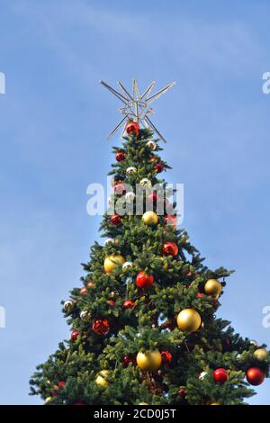 Geschmückter Weihnachtsbaum mit roten, goldenen und silbernen Weihnachtskugeln und einem silbernen Stern auf der Oberseite gegen einen blauen Himmel. Stockfoto