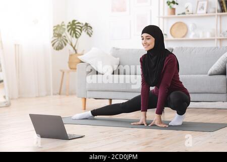 Sportliche muslimische Frau in Hijab Training zu Hause, Tutorials auf Laptop Stockfoto