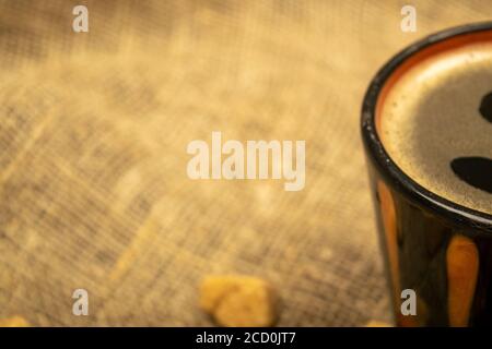 Tasse Kaffee und Scheiben braunen Rohrzuckers auf einem Hintergrund von homespun Stoff mit einer rauen Textur. Nahaufnahme Stockfoto