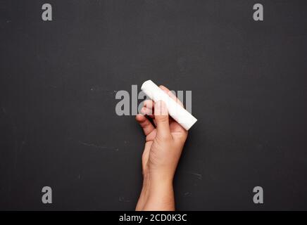 Hand hält ein Stück weiße Kreide auf dem Hintergrund eines leeren schwarzen Kreidetafel, Präsentationskonzept, zurück in die Schule Stockfoto