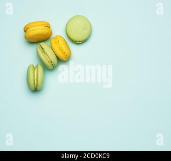 Gebackene gelbe und grüne Macarons Plätzchen liegen in einer Reihe auf blauem Hintergrund, Blick von oben Stockfoto