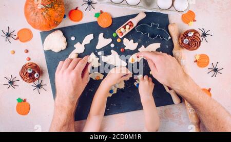 Familienurlaubsaktivität. Draufsicht auf Halloween-Cookies Dekoration von Vater und Kind Händen. Stockfoto