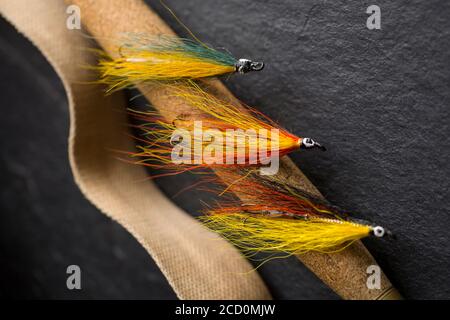 Drei Lachsfliegen, die wahrscheinlich auf dem Korkgriff einer alten Fliegenfischerrute neben dem Gurt aus einer Whicker-Tackle-Box hausgemacht waren. Aus einer Sammlung Stockfoto