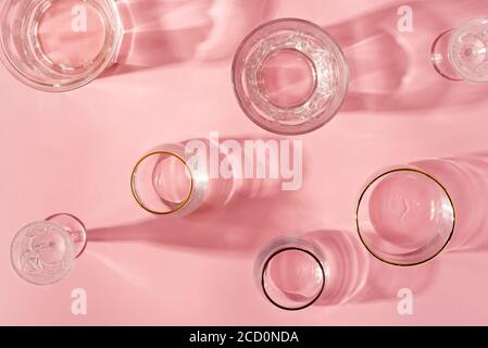 Draufsicht auf transparente leere Gläser für Wein auf einem pastellrosa Hintergrund mit weichen langen Schatten und Reflexionen, Kopierraum. Stockfoto