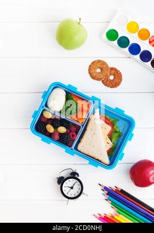 Offene Lunchbox mit Sandwich, Gemüse, Ei, frischen Beeren mit Uhr, Aquarell und Bleistiften auf weißem Holzhintergrund. Draufsicht, flach liegend. Stockfoto