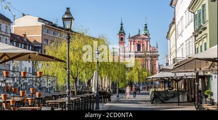 Rückansicht einer nicht erkennbaren Frau, die während einer Corona-Virus-Pandemie im alten mittelalterlichen Stadtzentrum von Ljubljana mit einem Hund unterwegs war. Leere Bars und Restaurants Stockfoto