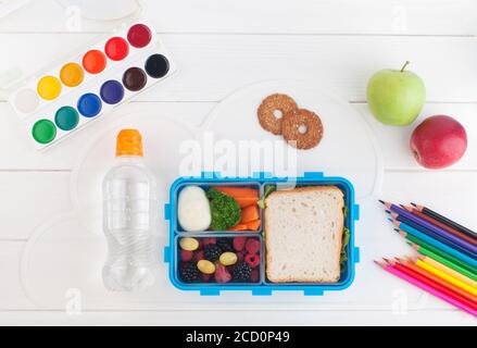 Offene Lunchbox mit Sandwich, Gemüse, Ei, frischen Beeren in der Nähe Wasserflasche auf dem weißen Holzhintergrund. Draufsicht, flach liegend. Stockfoto