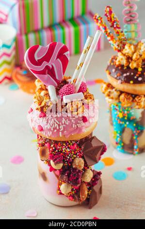 Draufsicht auf Himbeer-Freak-Shake-Belag mit Donut, Karamell-Popcorn und Süßigkeiten auf Party-Hintergrund; selektiver Fokus. Stockfoto