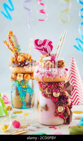 Kids Party Konzept: Raspberry Freak Shake Belag mit Donut und Karamell Popcorn und dekoriert mit Karamell und Milchschokolade auf Partytisch; selecti Stockfoto