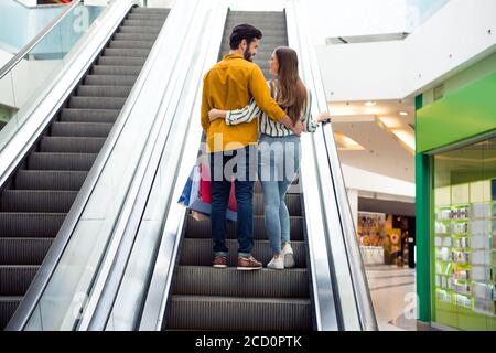 Rückseitenrückseite Rückseitenansicht Foto von zarten sanften zwei Personen Komfort gemütliche Harmonie Ehepartner bewegen Rolltreppe Umarmung Umarmung fühlen Bindung Pakete im Einkauf halten Stockfoto