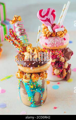 Kids Party Konzept: Zwei Freak-Shakes mit Donuts, Bonbons und Süßigkeiten auf dem Partytisch; selektiver Fokus. Stockfoto