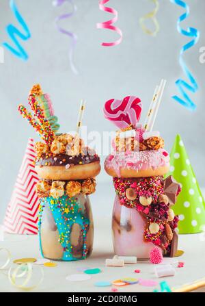 Zwei Freak-Shakes mit Donuts, Karamell-Popcorn und Süßigkeiten auf dem Kinderparty-Tisch; selektiver Fokus. Stockfoto