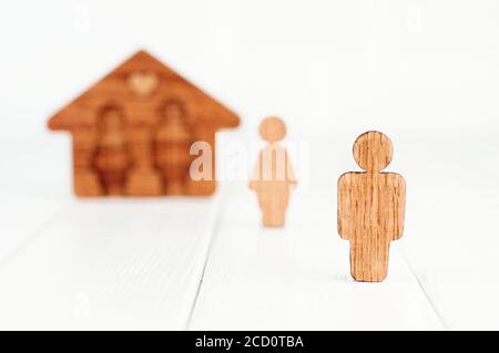 Hölzerne männliche Figur vor weibliche Figur und Haus auf weißem Hintergrund als Symbol für Probleme in Familienbeziehungen. Fokus auf männliche Figur, leer Stockfoto