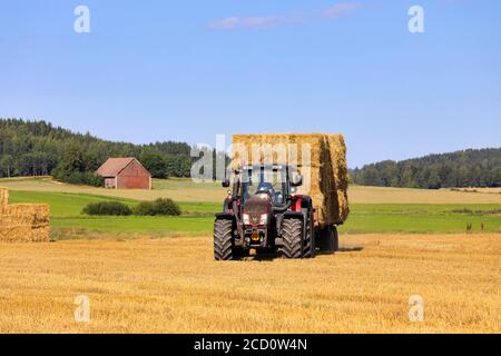 Transport von Strohballen mit Valtra Traktor und landwirtschaftlichen Anhänger von geerntetem Feld zur Lagerung im Spätsommer. Salo, Finnland. 16. August 2020. Stockfoto