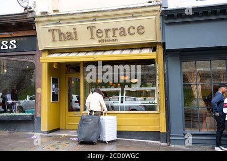 Windsor, Berkshire, Großbritannien - 25. August 2020. Eine obdachlose Dame rollt ihre weltlichen Besitztümer in zwei Koffern und schaut sehnsüchtig in einem Restaurantfenster auf das Buffetessen. Quelle: Maureen McLean/Alamy Live News Stockfoto