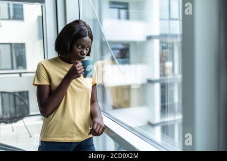 Afroamerikanische Frau in ihrem Wohnzimmer trinken hält eine Tasse Kaffee Tee - Menschen mit schwarzer Hautfarbe Stockfoto
