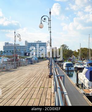 Sonnenscheinansicht von Yachten und Motorbooten, die am Pier in der Marina, Larnaca Stadtbild mit Resort-Hotels und Apartments im Hintergrund, Zypern Stockfoto