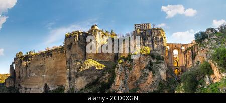 Ronda, Spanien: Landschaft der weißen Häuser am grünen Rand der steilen Klippen mit Bergen im Hintergrund. Stockfoto