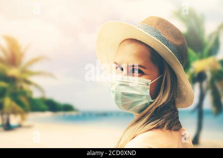 Junge Frau mit Schutzmaske am tropischen Strand. Covid-19 oder Coronavirus Pandemie. Sommerreise mit neuen normalen Stockfoto