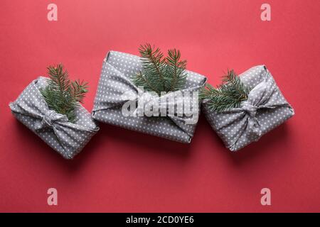 Nachhaltige Weihnachtsgeschenke in Textil auf Rot verpackt. Weihnachten. Japanischer Furoshiki-Stil. Blick von oben. Flach liegend. Stockfoto