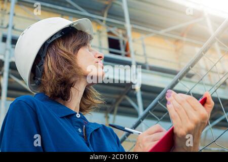 Frau, Ingenieurin, Kaukasierin, 40 Jahre alt, trägt eine weiße Sicherheitsmütze und arbeitet auf einer Baustelle in einer typischen Männerrolle. Symbol für geschlechtsspezifische Lücke. Stockfoto