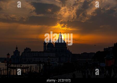 Silhouette der Santa Maria della Salute Hintergrundbeleuchtung, mit dem Himmel mit feurigen Wolken in der Lagune reflektieren Stockfoto