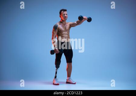 Sportler mit Behinderungen oder Amputee isoliert auf blauem Studiohintergrund. Profi-Sportlerinnen mit Beinprothesentraining mit Gewichten in Neon. Behinderten-Sport und Überwindung, Wellness-Konzept. Stockfoto