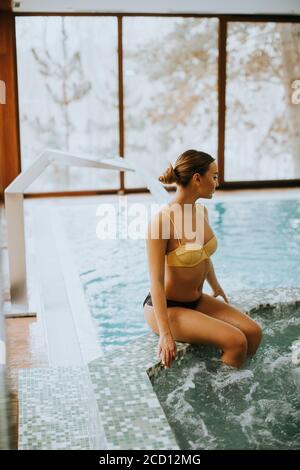 Hübsche junge Frau, die an der Whirlpool-Badewanne sitzt und sich entspannt Stockfoto