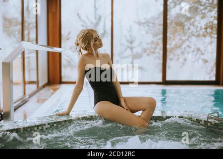 Hübsche junge Frau, die an der Whirlpool-Badewanne sitzt und sich entspannt Stockfoto