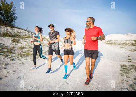 Gruppe von Läufern joggt im Freien auf weißem Gelände. Weitwinkelansicht mit langen Schatten Stockfoto