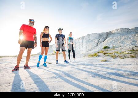 Gruppe von Läufern, die vor dem Trailrunning-Training im Freien stehen. Weitwinkelansicht mit langen Schatten Stockfoto