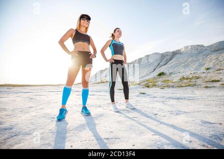 Zwei junge Fitness-Frauen stehen im Wüstengelände gegen die Sonne. Konzeptbild des sportlichen Lebensstils Stockfoto