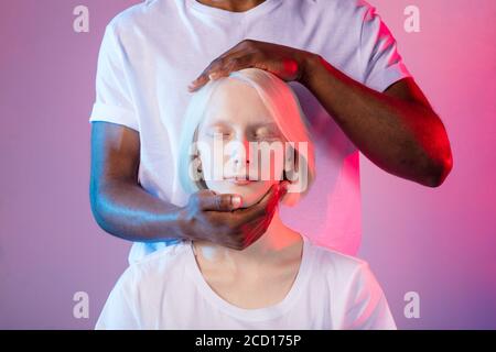 Die Hände des Mannes liegen auf dem Kopf der Frau. Guy massiert den Kopf des Patienten. Gesundheit und Körperpflege, magische Behandlung. Nahaufnahme Foto. Isoliert rosa Hintergrund Stockfoto