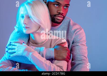 Junge multirassische Paar umarmt über isolierten blauen Hintergrund, Mann schützt seine Freundin vor schlechten Menschen, Liebe, Beziehung Stockfoto