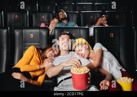 Junge Menschen schlafen während langweiligen Film im Kino, onlu ein blonder Kerl essen Popcorn und Film.close up Foto. Schlechter Film Stockfoto