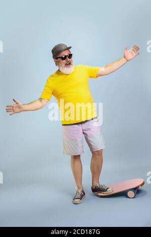 Skater Mann. Portrait von Senior Hipster Mann in Brille isoliert auf hellblauen Studio Hintergrund. Tech und fröhliche ältere Lifestyle-Konzept. Trendige Farben, für immer Jugend. Copyspace für Ihre Anzeige. Stockfoto