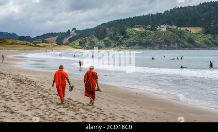 Buddhistische Mönche, die auf dem Sand des Hot Water Beach spazieren. Ein unterirdischer Fluss von heißem Wasser fließt aus dem Inneren der Erde an die Oberfläche im Pac... Stockfoto