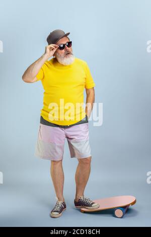 Skater Mann. Portrait von Senior Hipster Mann in Brille isoliert auf hellblauen Studio Hintergrund. Tech und fröhliche ältere Lifestyle-Konzept. Trendige Farben, für immer Jugend. Copyspace für Ihre Anzeige. Stockfoto