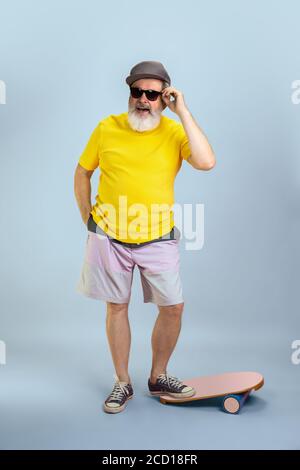 Skater Mann. Portrait von Senior Hipster Mann in Brille isoliert auf hellblauen Studio Hintergrund. Tech und fröhliche ältere Lifestyle-Konzept. Trendige Farben, für immer Jugend. Copyspace für Ihre Anzeige. Stockfoto