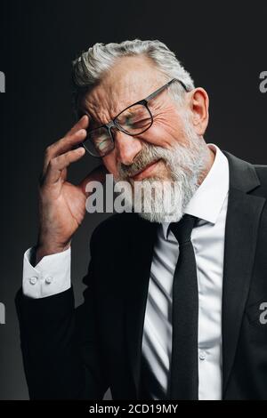 Senior Geschäftsmann in seinen 70ern mit grauen Haaren und Bart, Kopfschmerzen und reiben Schläfen, Blick auf die Kamera mit müden schmerzhaften Augen, isoliert über Stockfoto