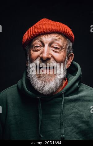 Grauhaariger Großvater im Alter fühlt sich überglücklich und aufgeregt, während er von seiner Reise in die Berge erzählt. Alter Mann in rot gestrickt Hut und grün ho gekleidet Stockfoto