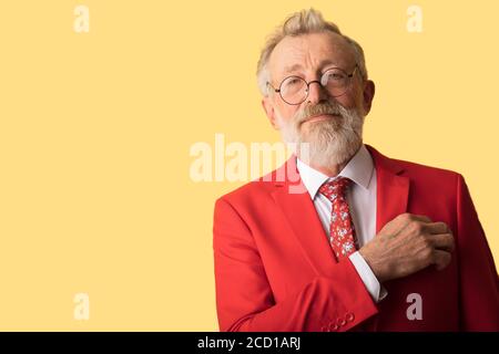 Portrait von erfolgreichen Modedesigner in Luxus stilvolle roten Anzug mit Krawatte Blick auf die Kamera gekleidet, während über gelben Hintergrund. Stockfoto