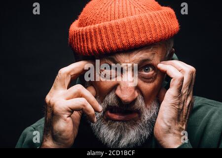 Emotionaler alter Mann, der die Hände an Tempeln hält und die Kamera mit einem verrückten, verstupten, unzufriedeneren Ausdruck anschaut, als ob er schlechte Nachrichten von smb hört und versucht, mich zu nehmen Stockfoto