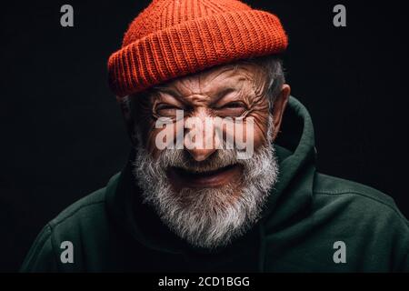 Grauhaariger Großvater im Alter fühlt sich überglücklich und aufgeregt, während er von seiner Reise in die Berge erzählt. Alter Mann in rot gestrickt Hut und grün ho gekleidet Stockfoto
